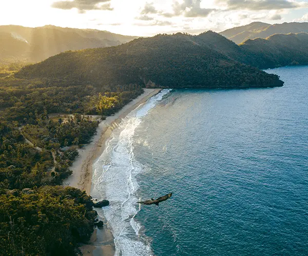 A plane flying over the ocean near mountains.