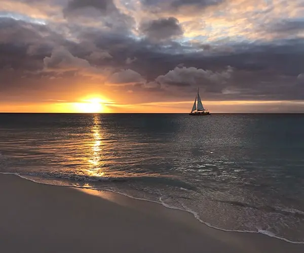 A sailboat is sailing on the ocean at sunset.