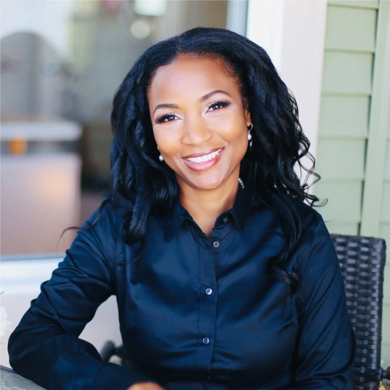 A woman sitting at an outdoor table smiling for the camera.