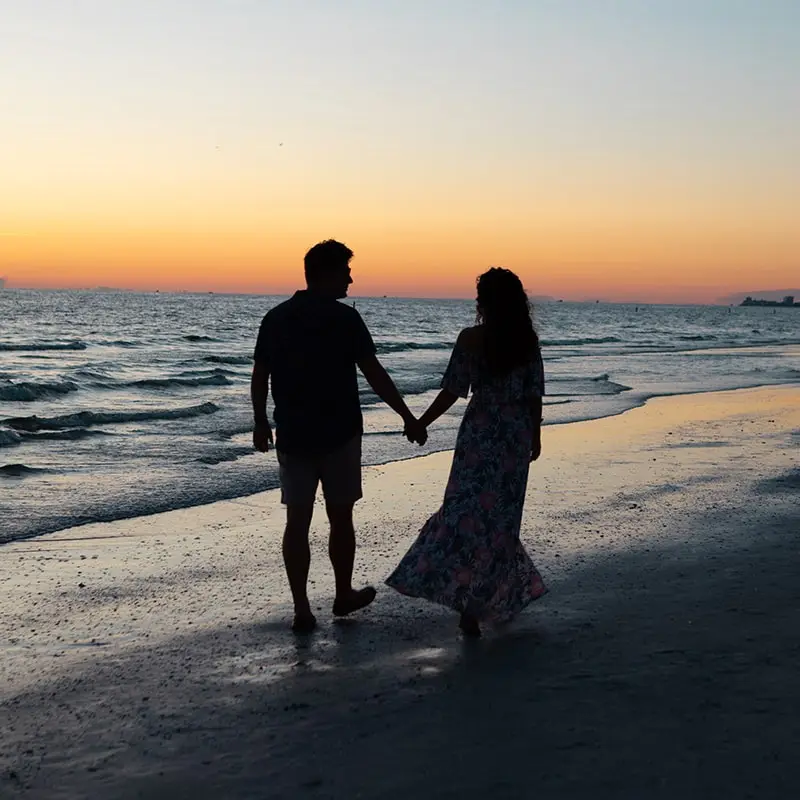 A man and woman holding hands on the beach.