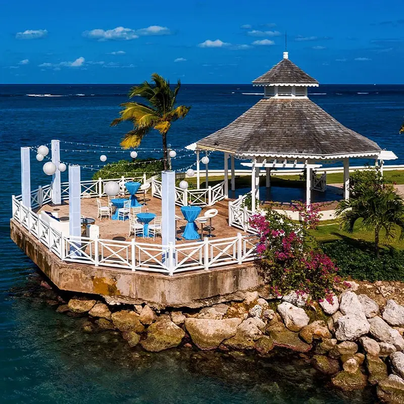 A gazebo with chairs and umbrellas on the water.