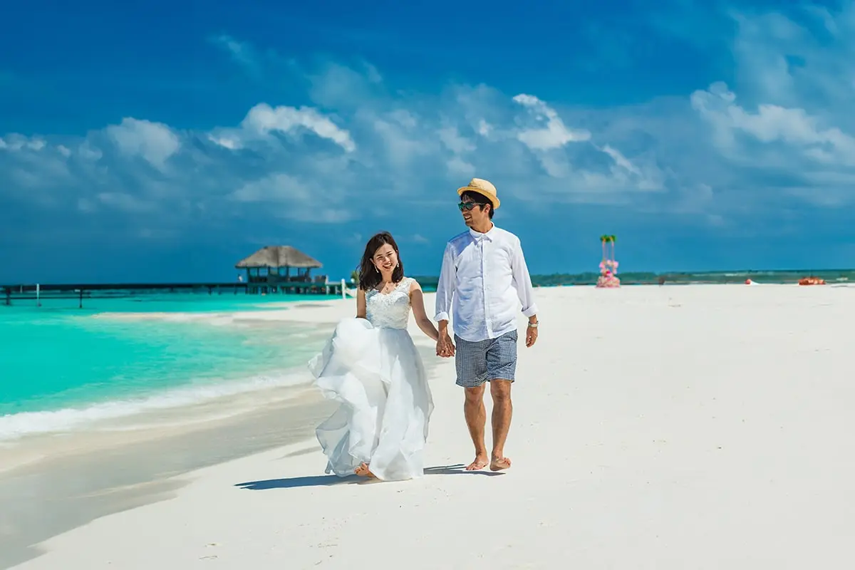 A man and woman holding hands on the beach.