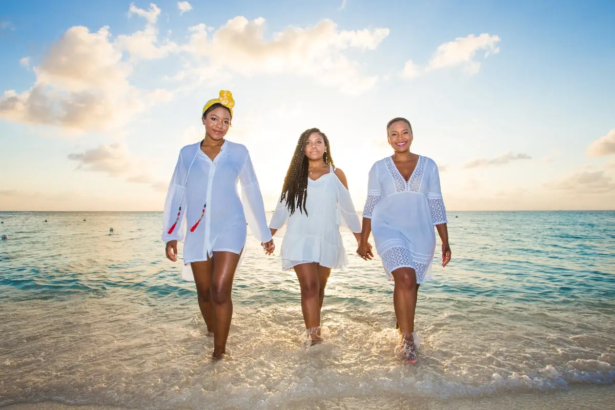 Three women walking on the beach holding hands.