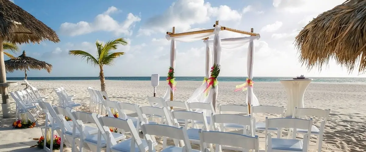 A beach wedding with white chairs and an arbor.