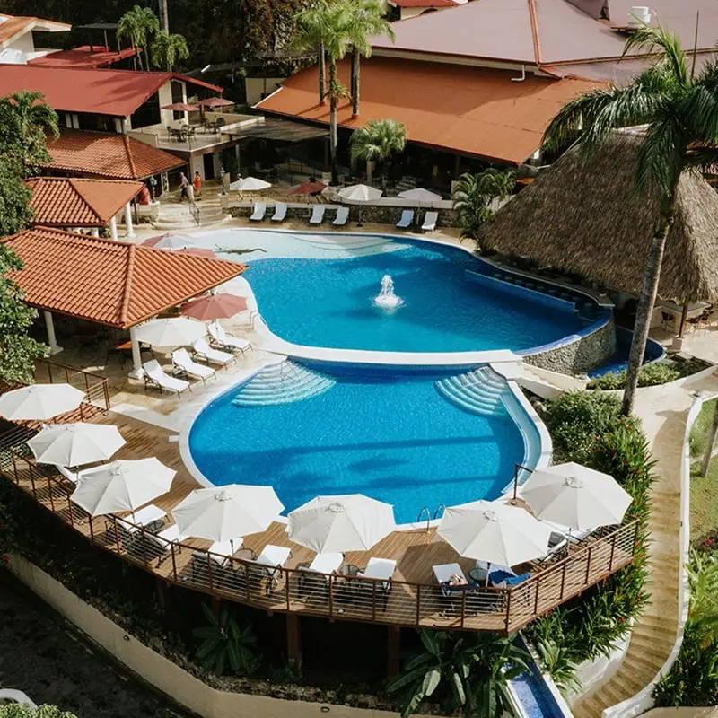 A resort pool with umbrellas and chairs in the background.