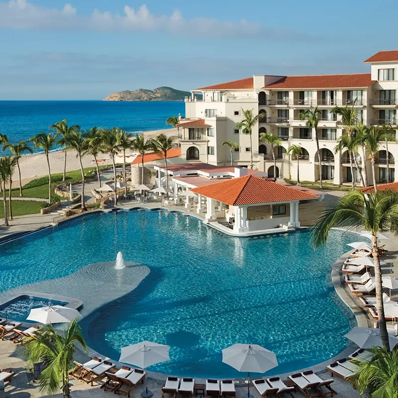 A resort with a pool and beach in the background.