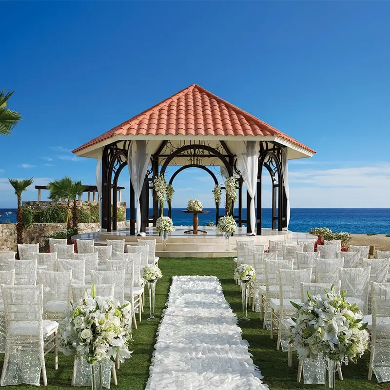 A wedding ceremony with white chairs and flowers.