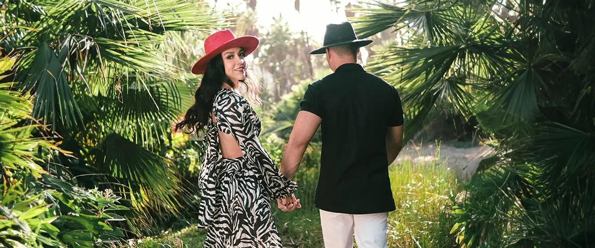 A man and woman holding hands while walking through the woods.