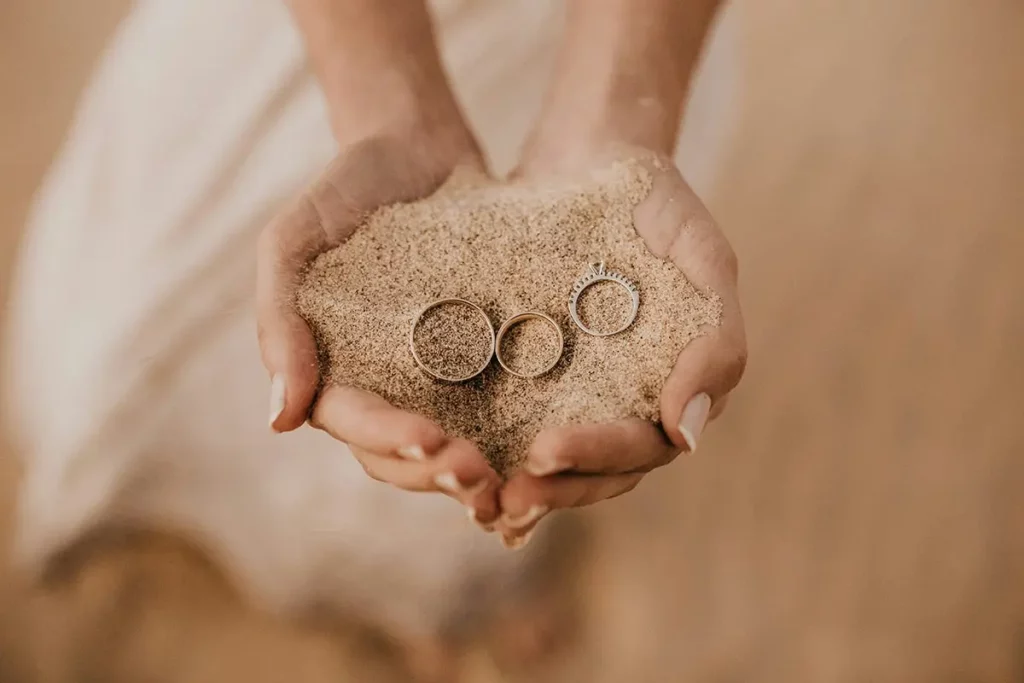 A person holding sand and two rings in their hands.