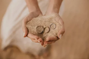 A person holding sand and two rings in their hands.