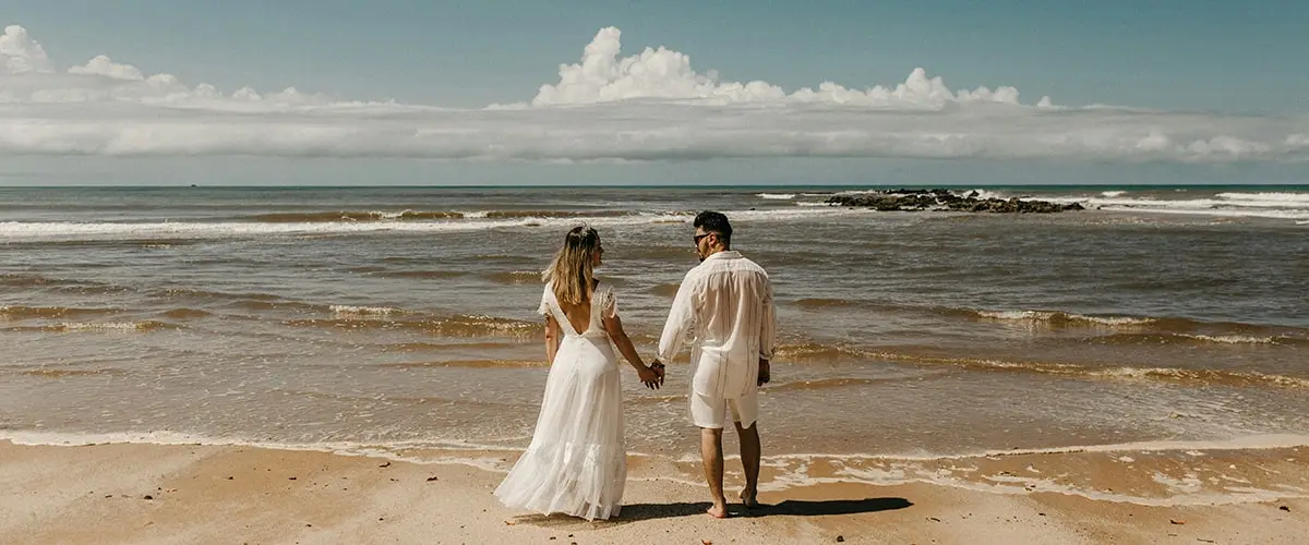 A man and woman holding hands on the beach.