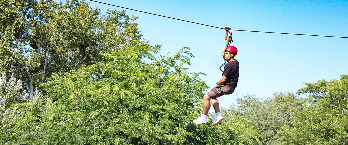 A man is hanging on to a rope while riding a zip line.