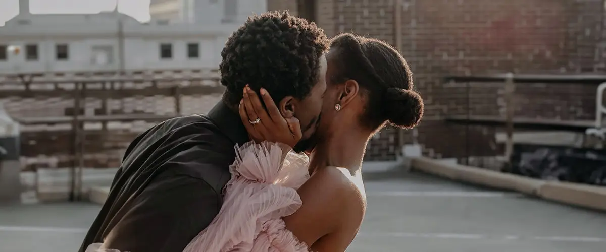 A man and woman kissing in front of some buildings.