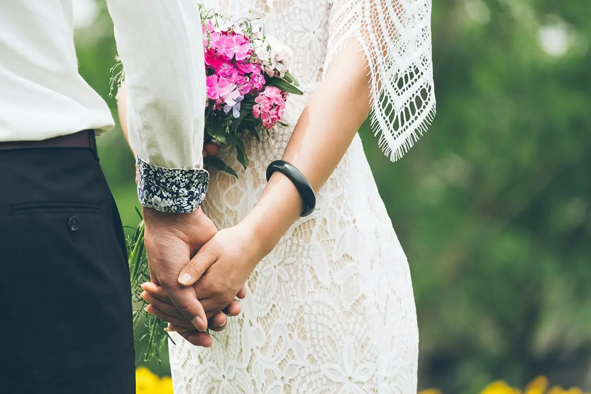 A man and woman holding hands in front of flowers.