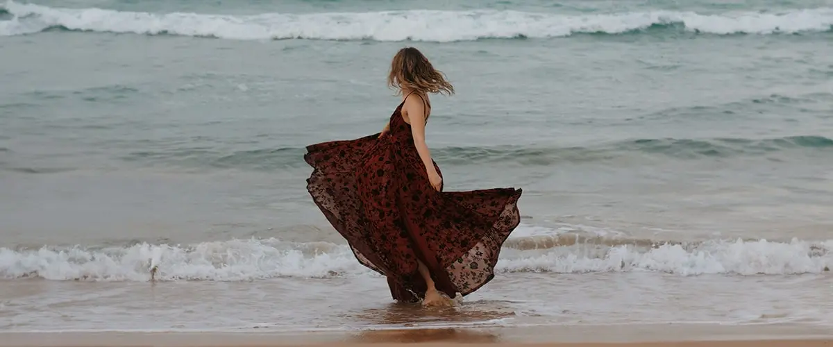 A woman in a dress is walking on the beach